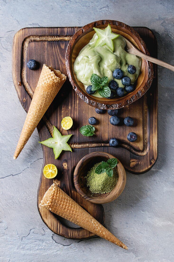 Bowl of Green tea matcha soft elastic ice cream with mint leaves, carambola, lime, blueberries and waffle cones