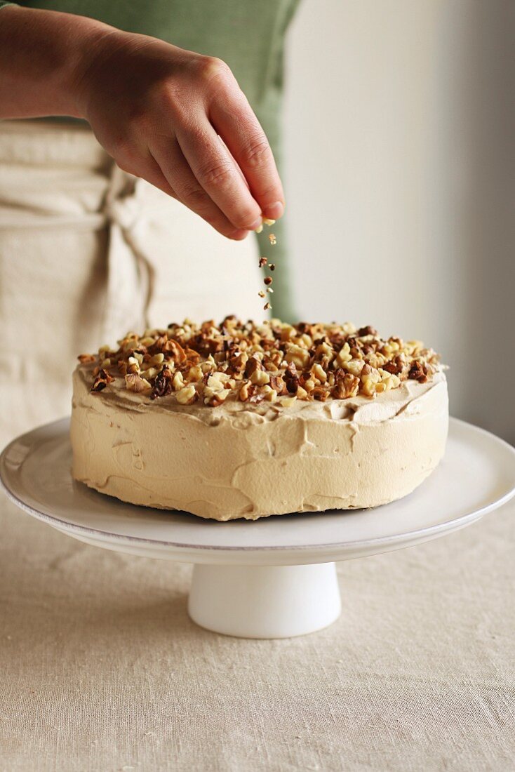 A woman sprinkling nuts on top of an iced cake