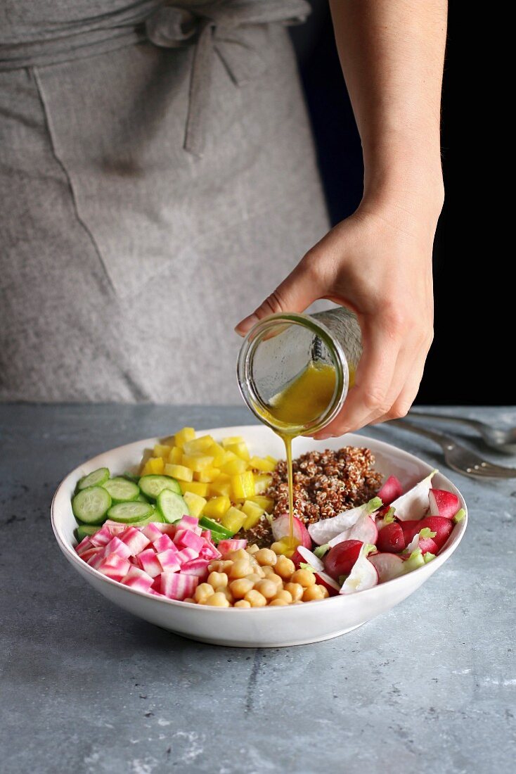 Hand pouring dressing over a quinoa salad with vegetables and chickpeas