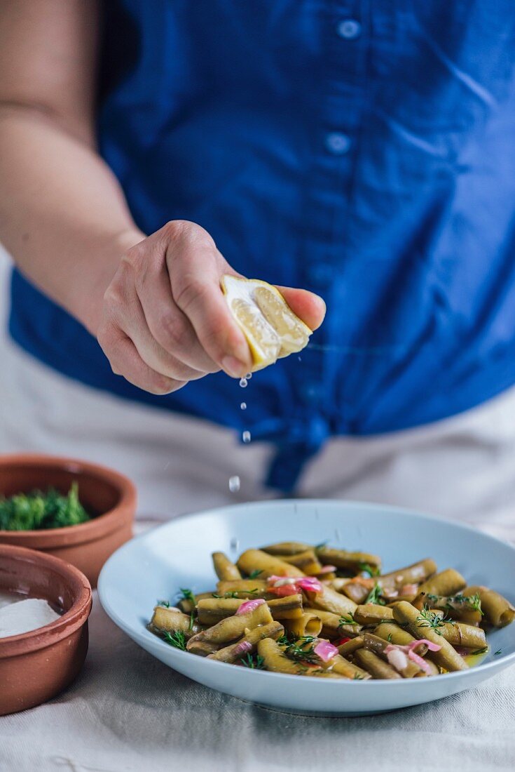 Frau beträufelt mediterranen Favabohnensalat mit Zitronensaft