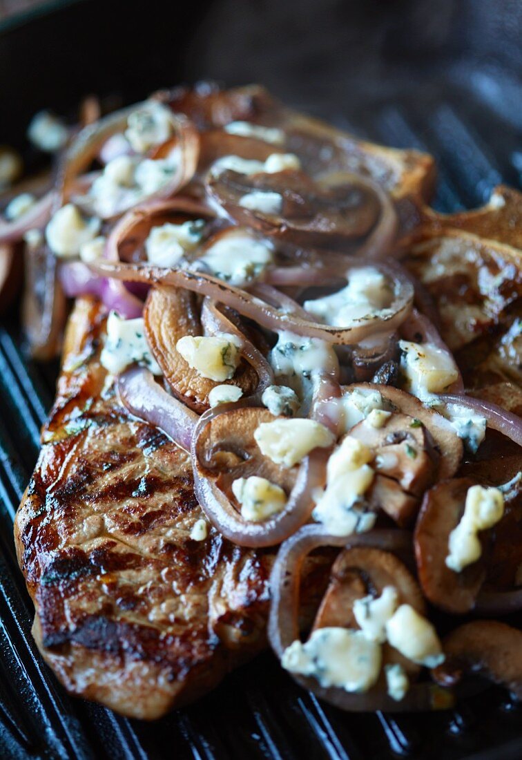 T-bone steak with onions and blue cheese on a grill