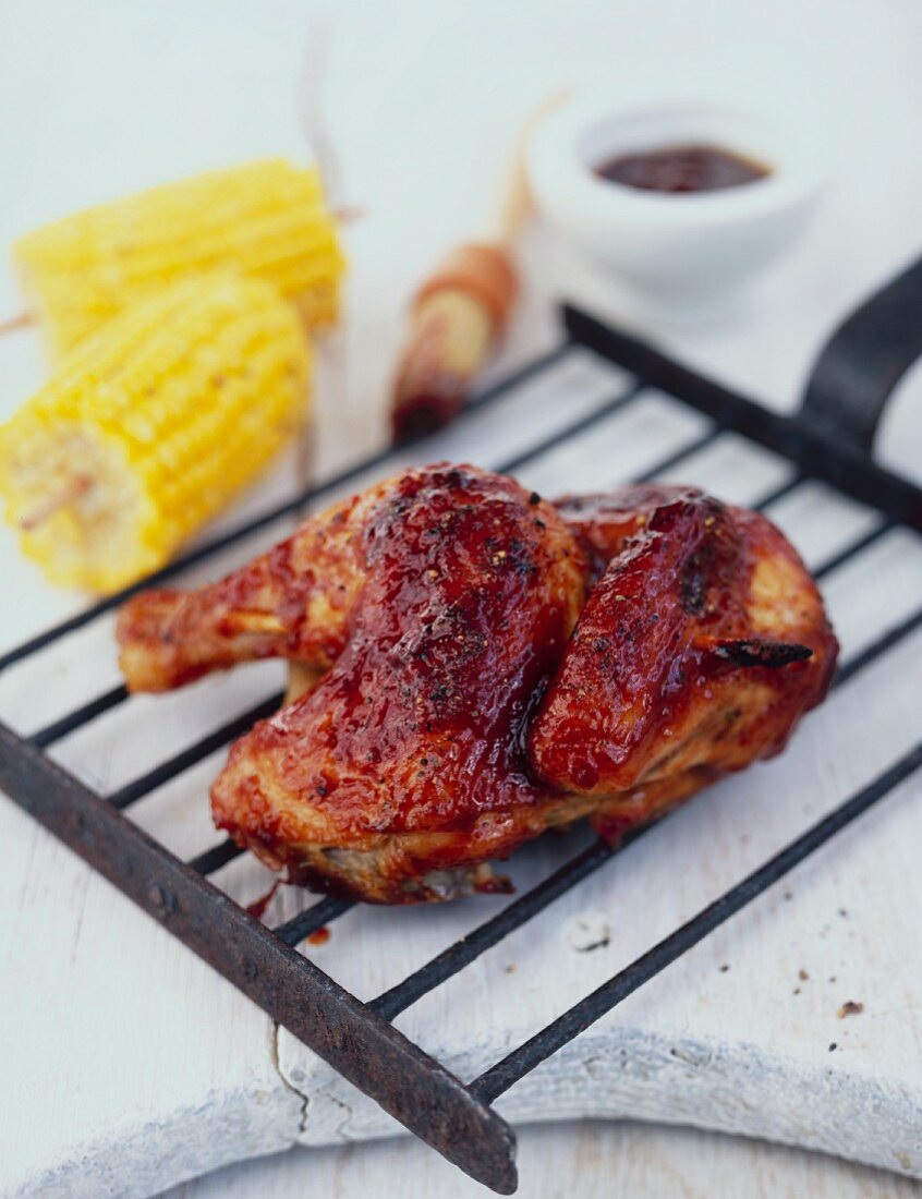 Half a BBQ chicken on a grill tray, with corn cobs and BBQ sauce