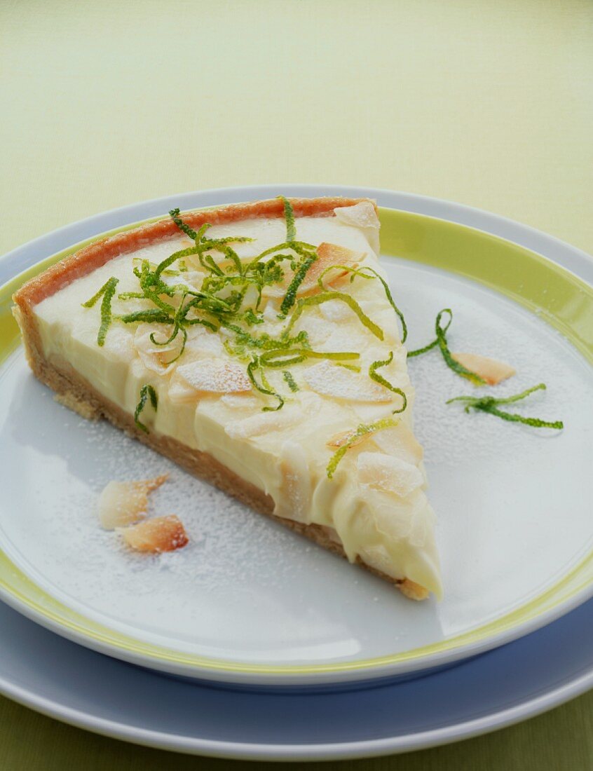 A slice of lemon tart with lime zest and coconut chips