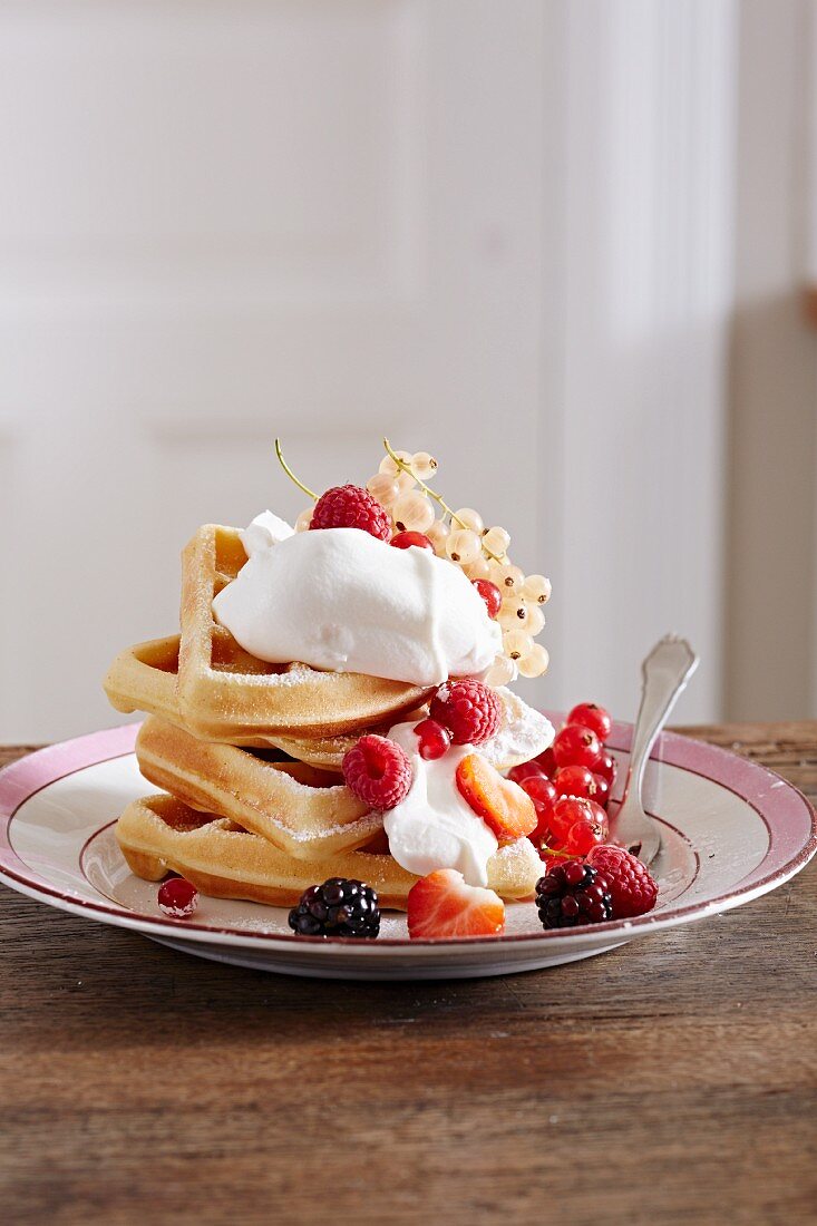 A stack of waffles with cream and fresh berries on a plate