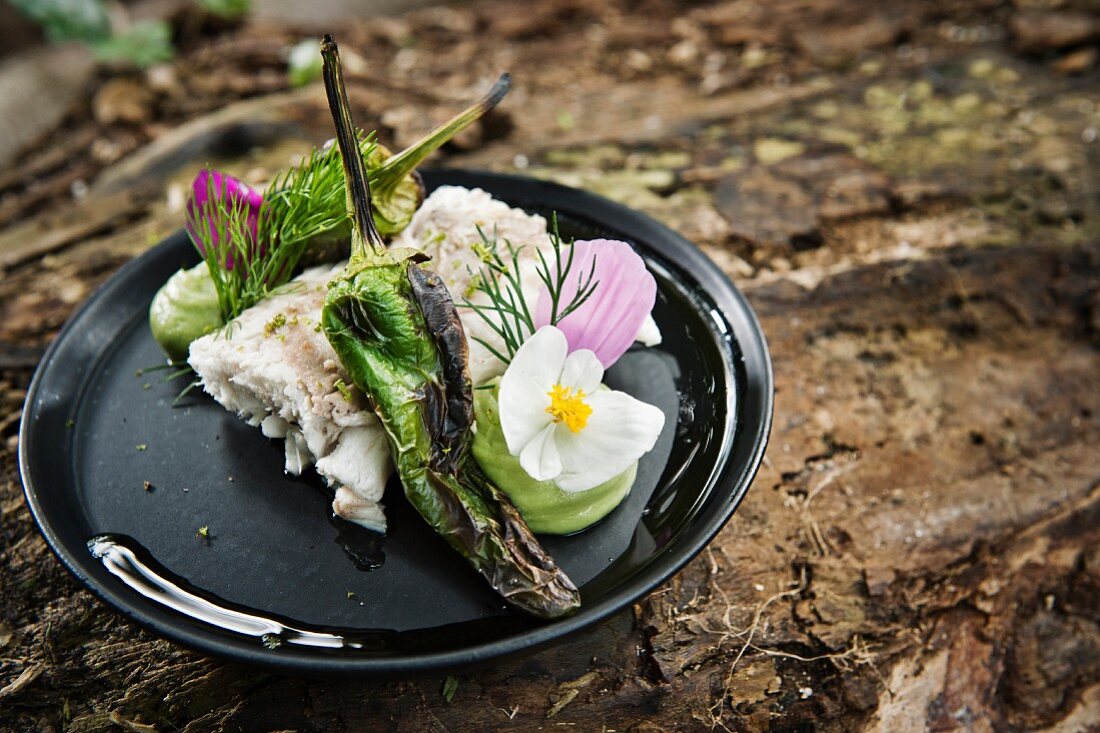 Fischfilet mit gegrillter Chilischote dekoriert mit Blüten fürs Camping