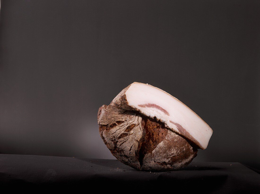 Half a loaf of bread and a piece of white bacon in front of a black background
