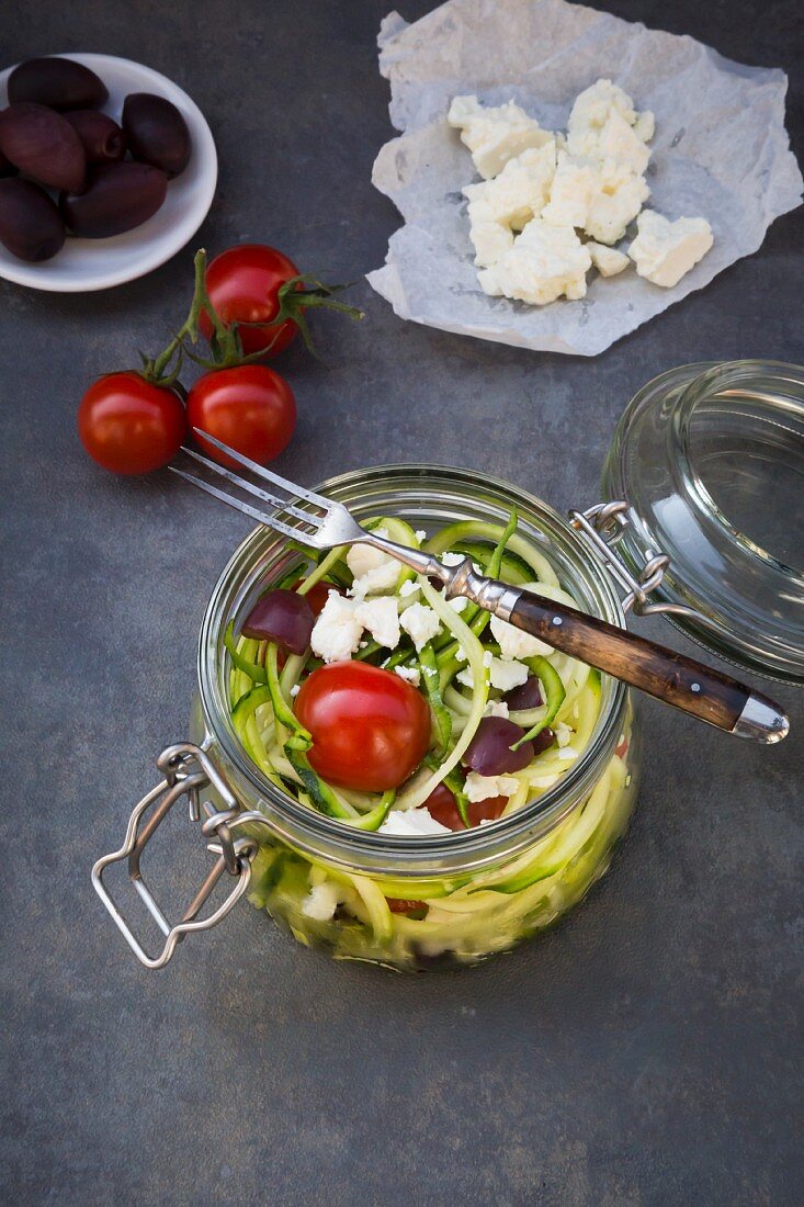 Zoodles (zucchini noodles) in a glass jar with tomatoes, feta and olives