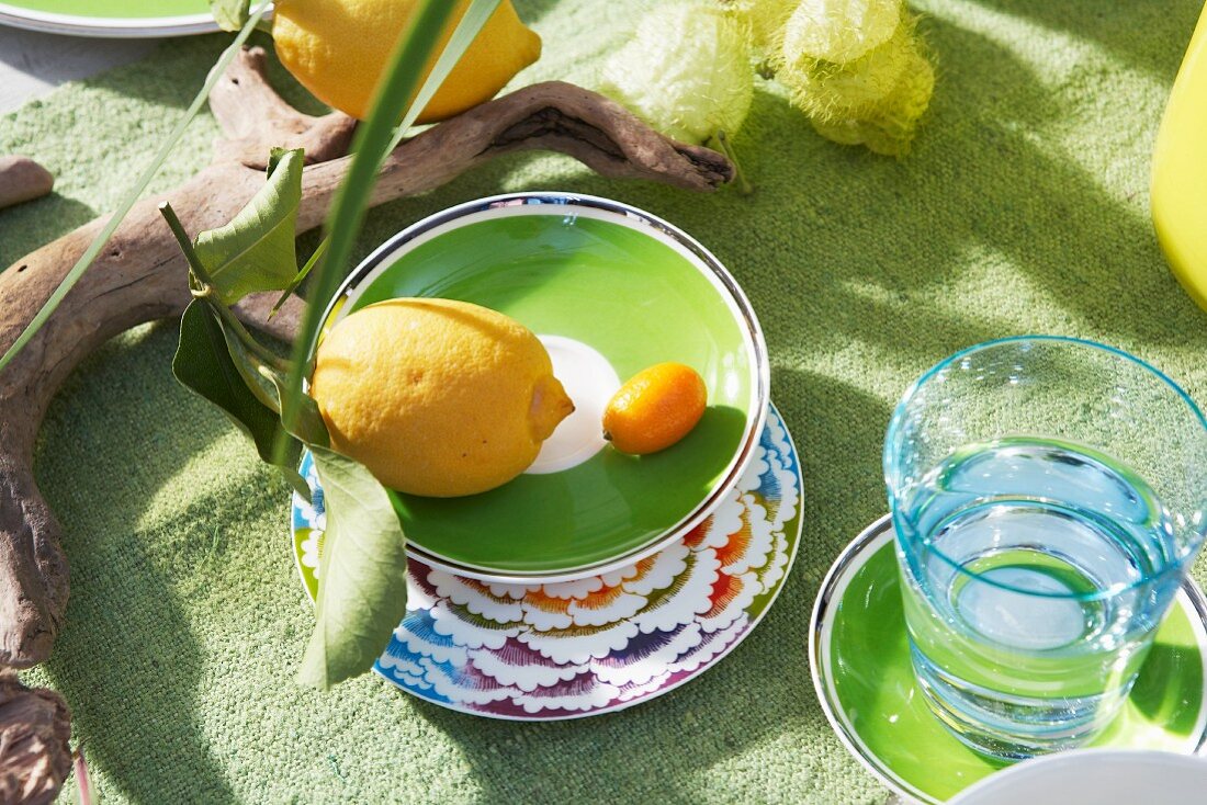 A lemon and a kumquat in a green bowl next to a water glass