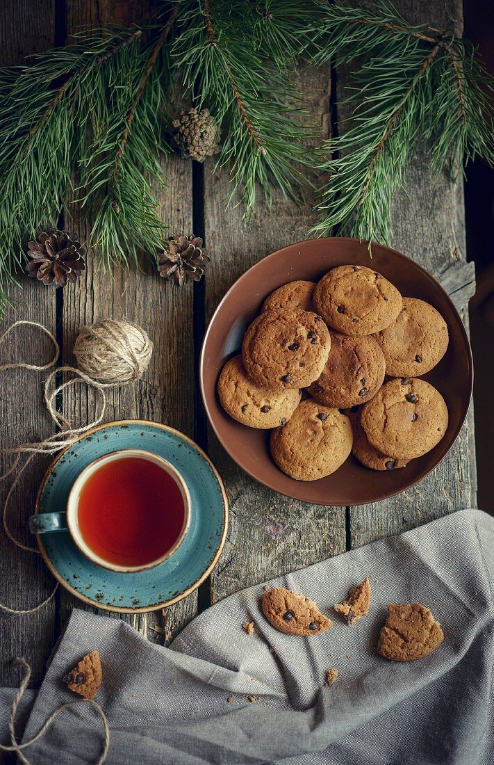 Chocolate Chip Cookies und eine Tasse Tee auf Holztisch mit Tannenzweigen