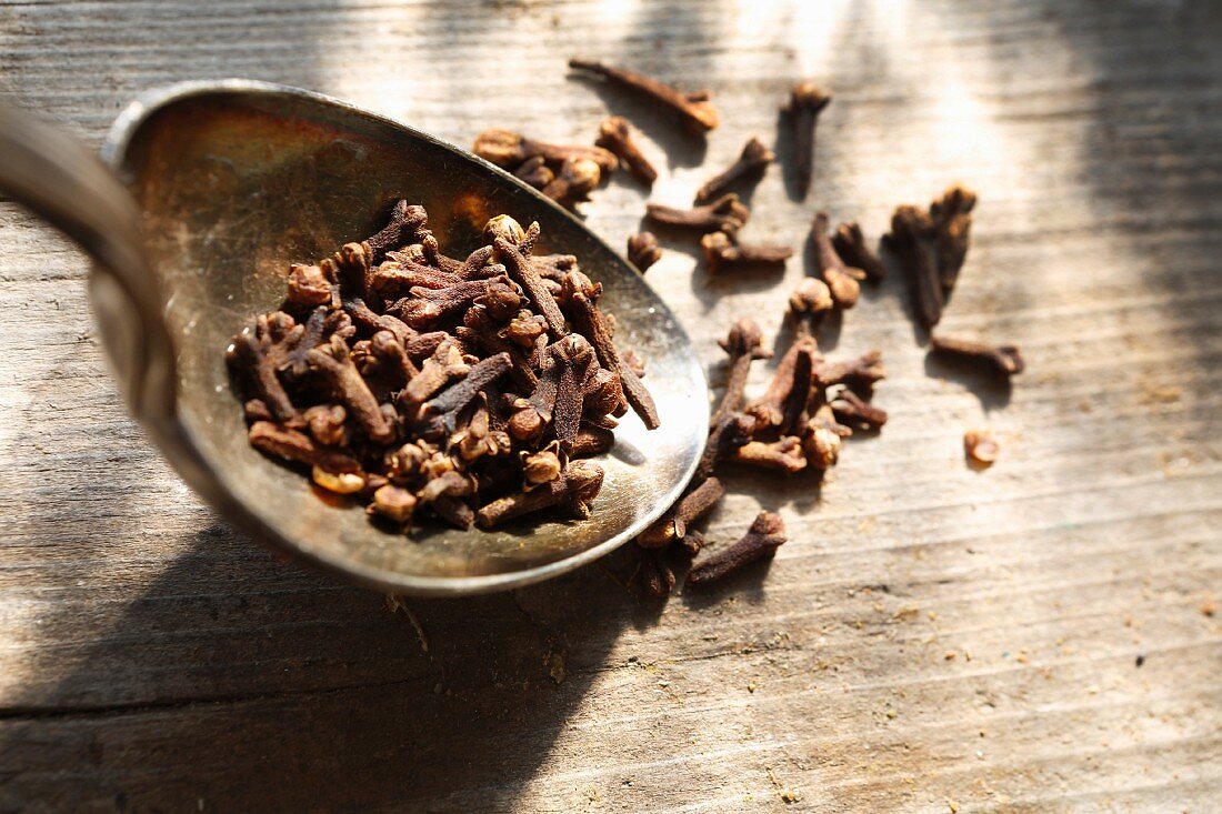 Cloves on and next to a silver spoon on a wooden surface