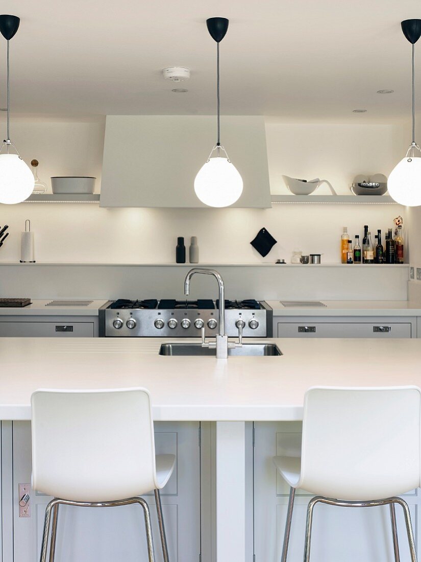 White counter with sink and bar stools in white kitchen with various lighting