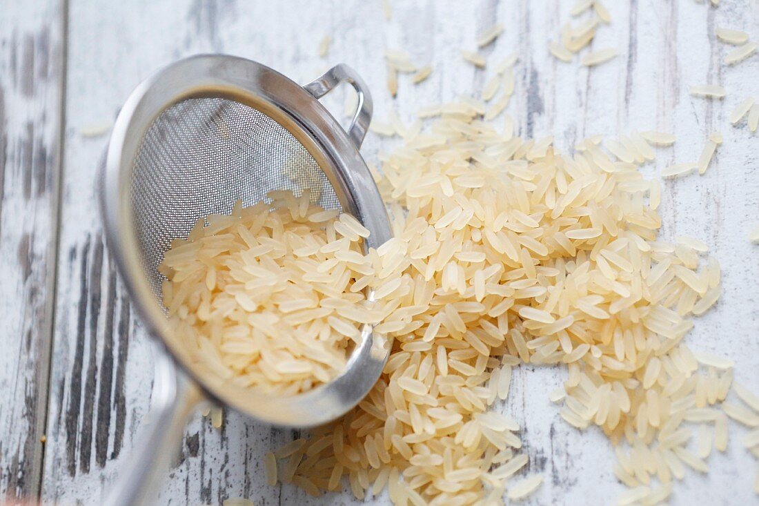 Long-grain rice in a sieve and on a wooden background