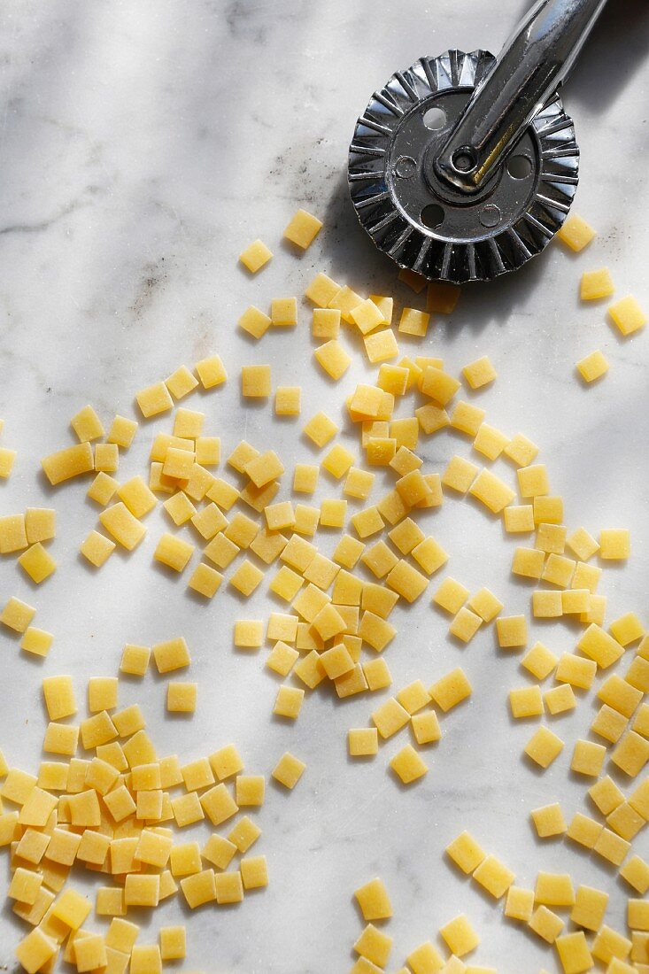 Uncooked square-shaped pasta with a pastry cutter on a marble background