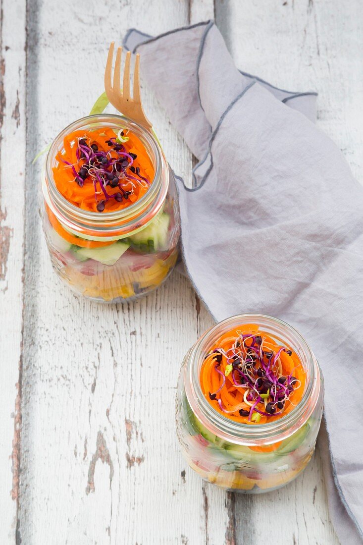 Rainbow salad in glass jars with red cabbage, yellow pepper, tomato, cucumber, carrots and beetroot sprouts