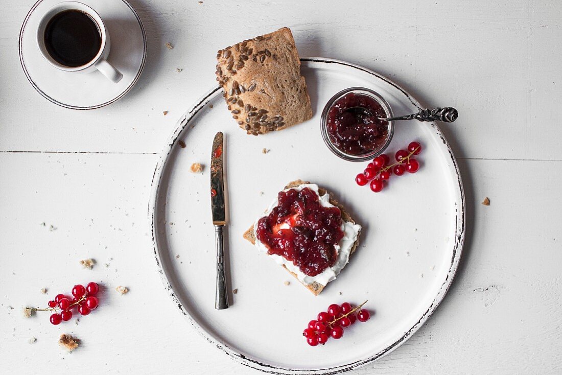 Marmeladenbrot auf weißem Holzbrett, dazu eine Tasse Kaffee (Aufsicht)