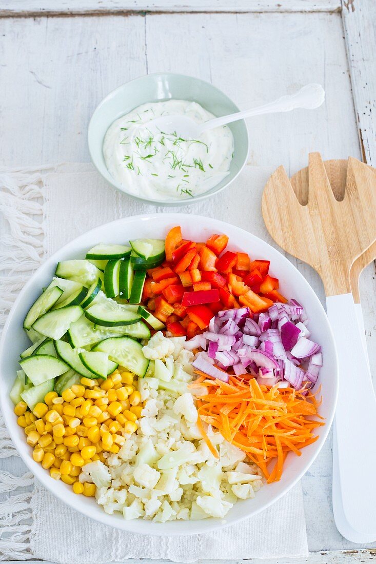 Chopped vegetables in a bowl with a dish of yoghurt and dill dressing next to it