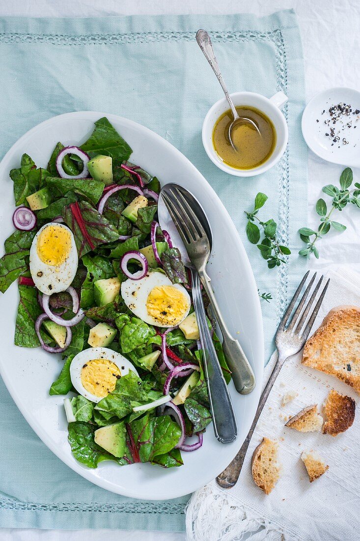 Spinatsalat mit gekochten Eiern, Zwiebeln, Avocado und Vinaigrette