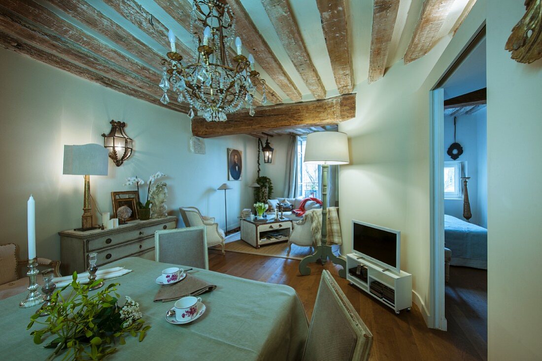 Offener Wohnraum in restaurierter Altbauwohnung mit rustikaler Holzbalkendecke, Kronleuchter und antiken Möbeln