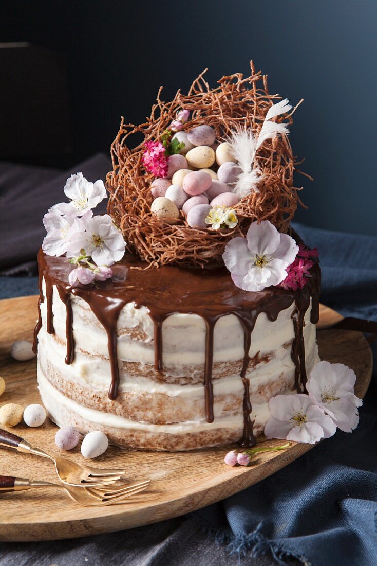A naked sponge cake decorated with an Easter nest, chocolate eggs and blossoms
