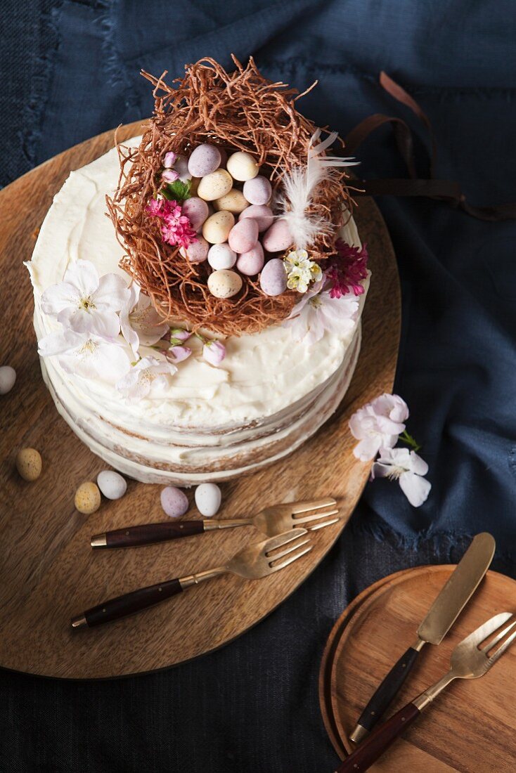 A naked sponge cake decorated with an Easter nest, chocolate eggs, and blossoms