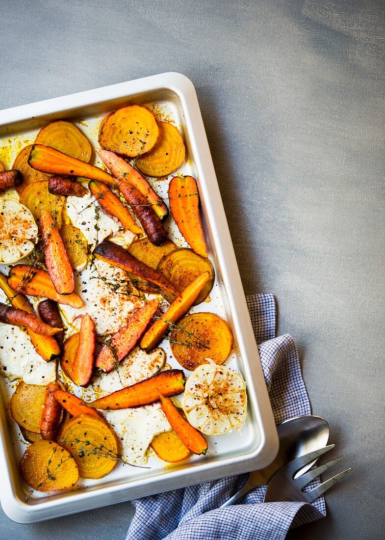 Roast vegetables with goat's cheese, garlic and herbs on an oven tray