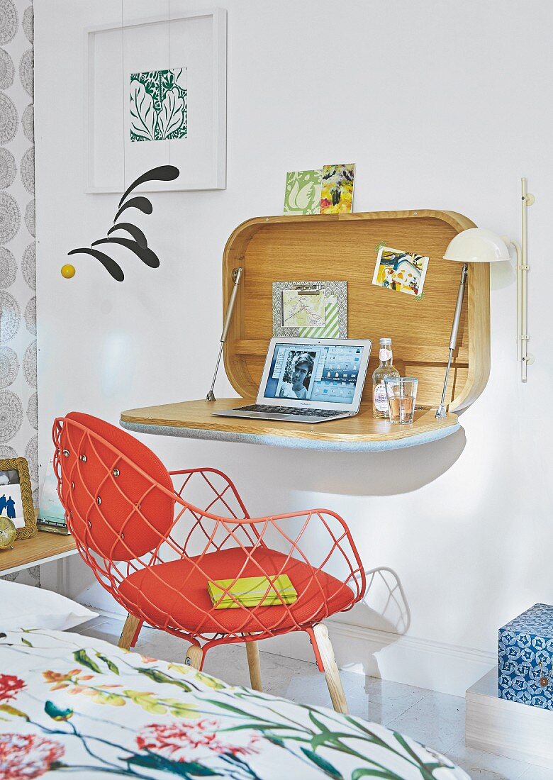 A bureau attached to the wall and a red designer chair in a bedroom