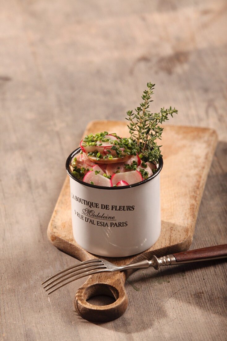 Sausage salad with radishes and thyme in an enamel mug