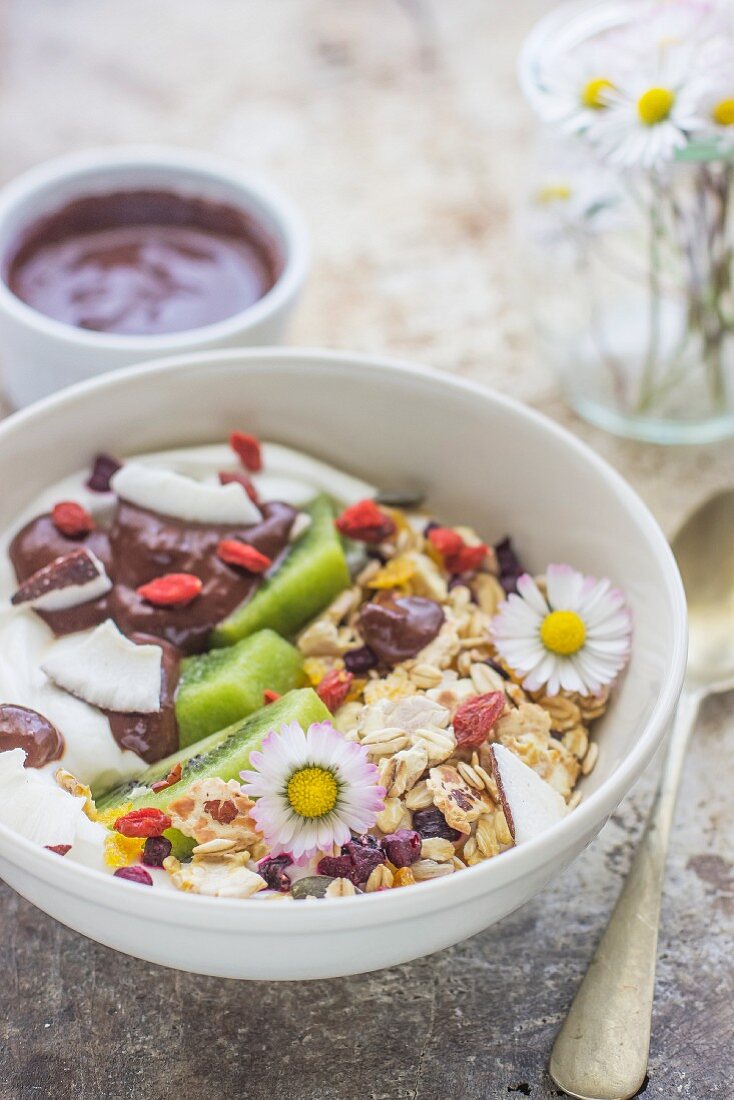 Joghurtmüsli mit Schokolade, Früchten und Gänseblümchen