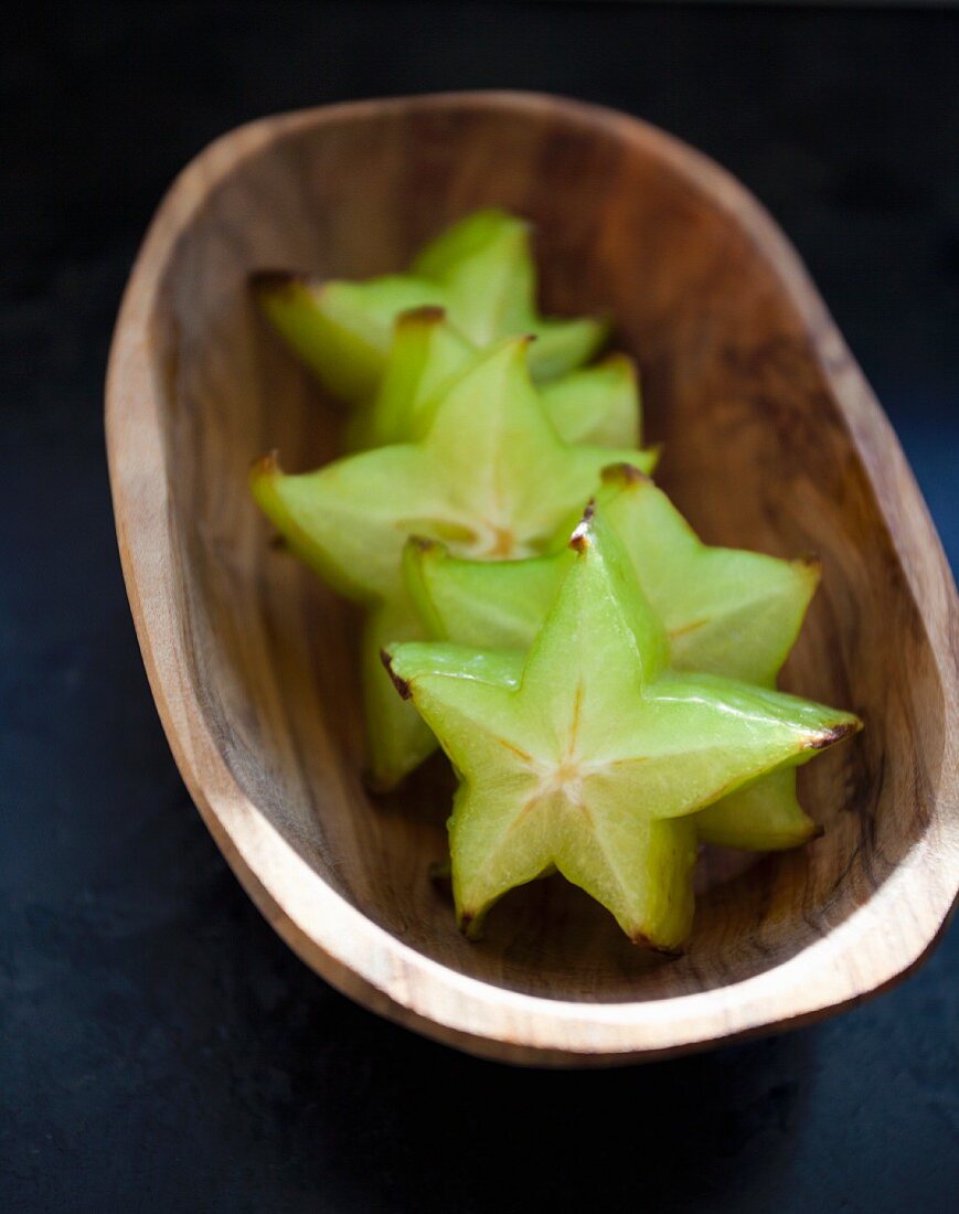 Starfruit in a small wooden bowl on a black countertop