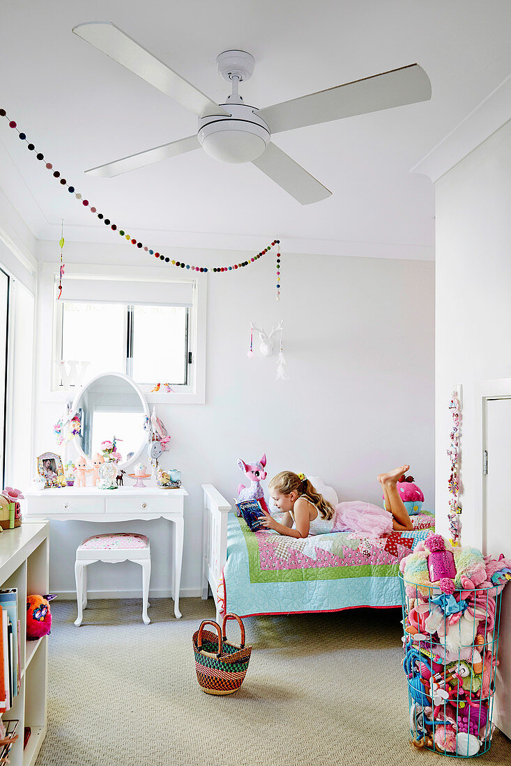 White children's room with colorful accessories, girl lies on bed with book