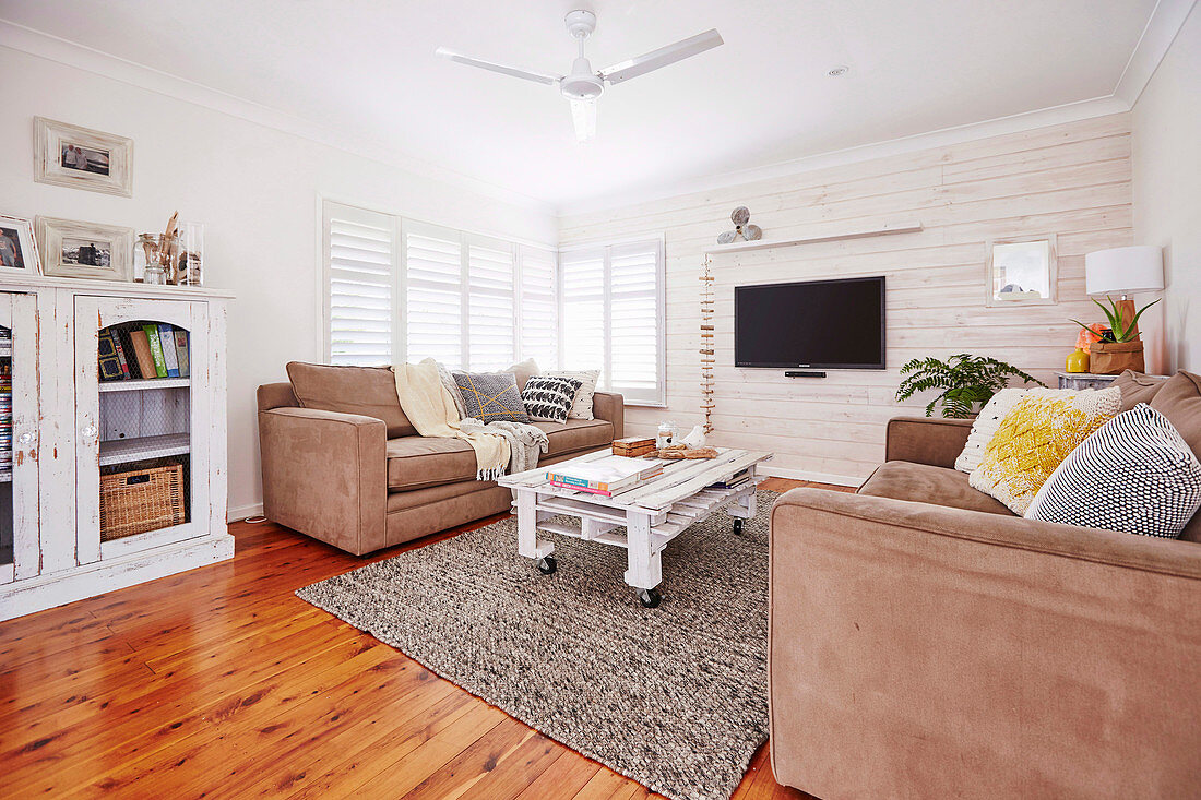 Polstergarnitur und rollbarer Palettentisch im Wohnraum mit weiss gestrichener Holzwand