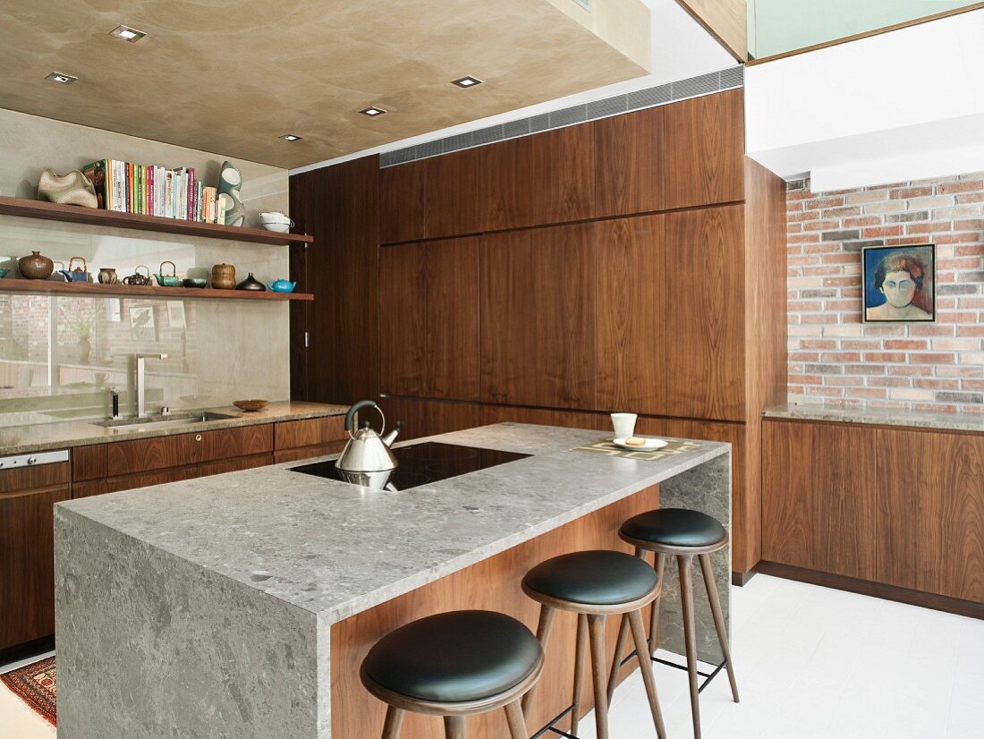 Island counter, delicate bar stools and fitted cupboards with exotic-wood fronts next to restored brick wall