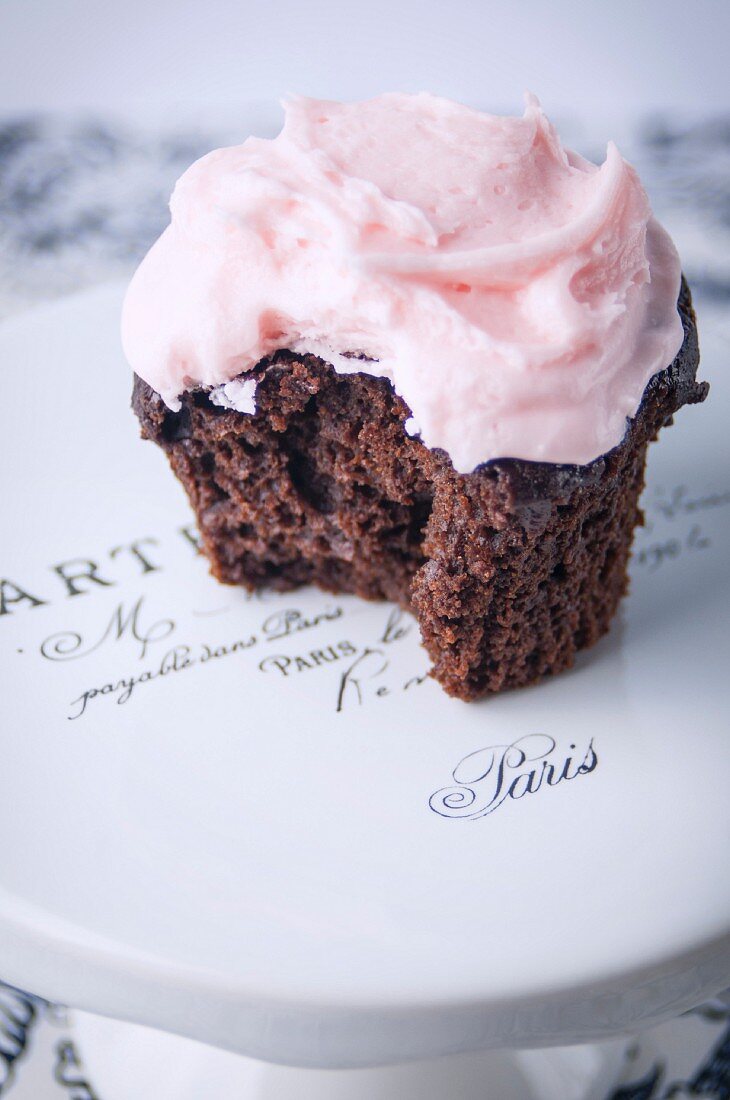 A Single Chocolate Cupcake with Pink buttercream Frosting with Bite Taken Out on Cakestand