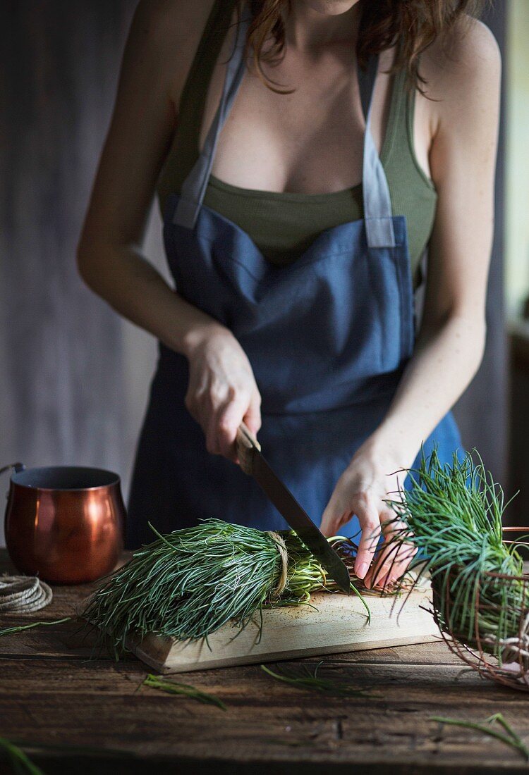Frau schneidet Agretti (Salzkraut, Italien) mit Messer auf Holzschneidebrett