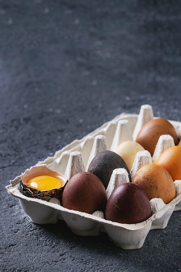 Brown and gray colored chicken Easter eggs in paper box with yolk over black concrete texture background