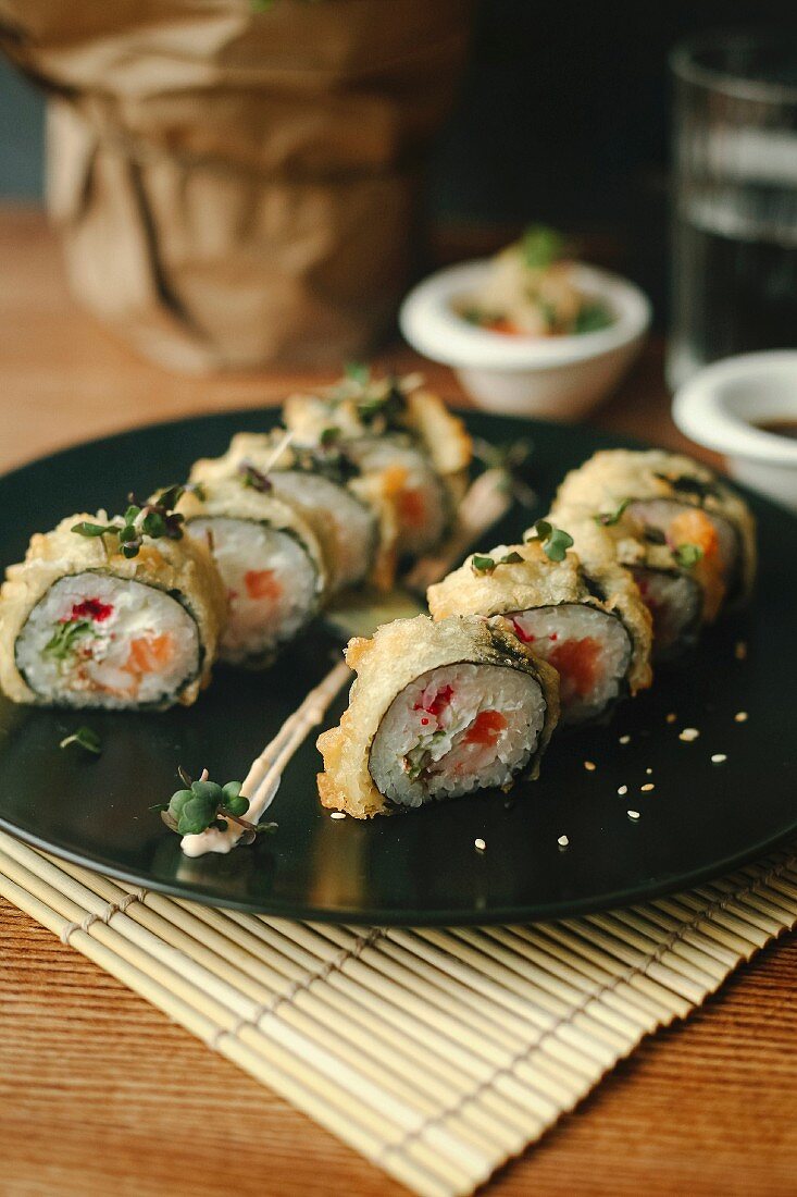 Sushi rolls with salmon, deep fried in tempura batter, on a black plate
