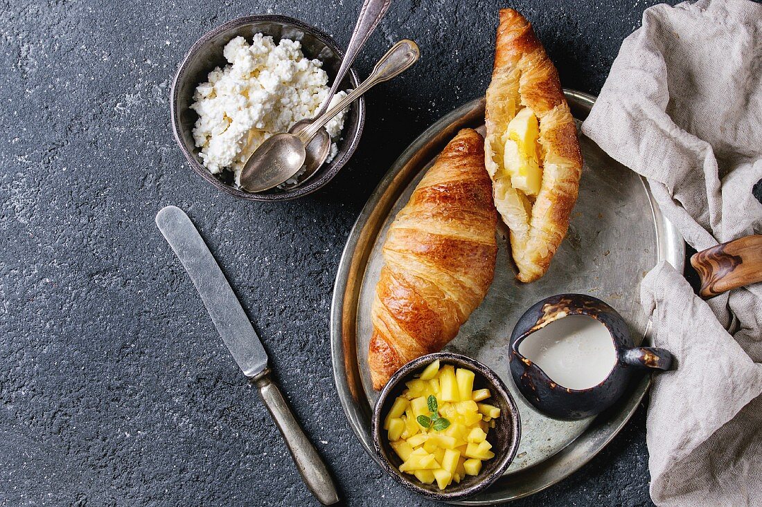 Breakfast with two croissant, butter, cottage cheese, cream, sliced mango fruit