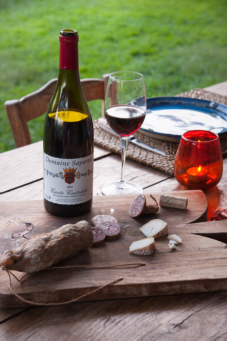 Wein und Holzbrett mit Salami und Käse auf dem Tisch im Garten