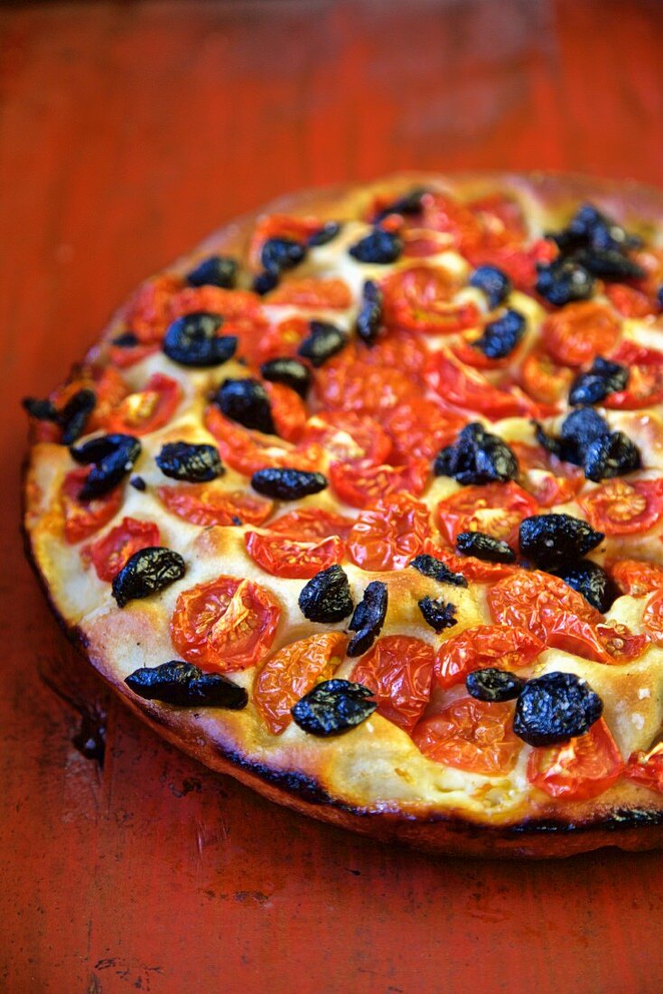 Focaccia mit Tomaten und Oliven auf rotem Holztisch (Italien)