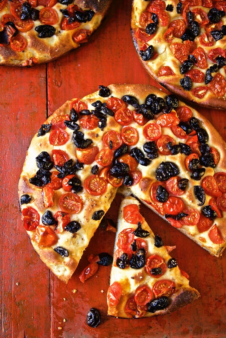 Focaccia with Tomatoes and Olives on a red table (Italy)