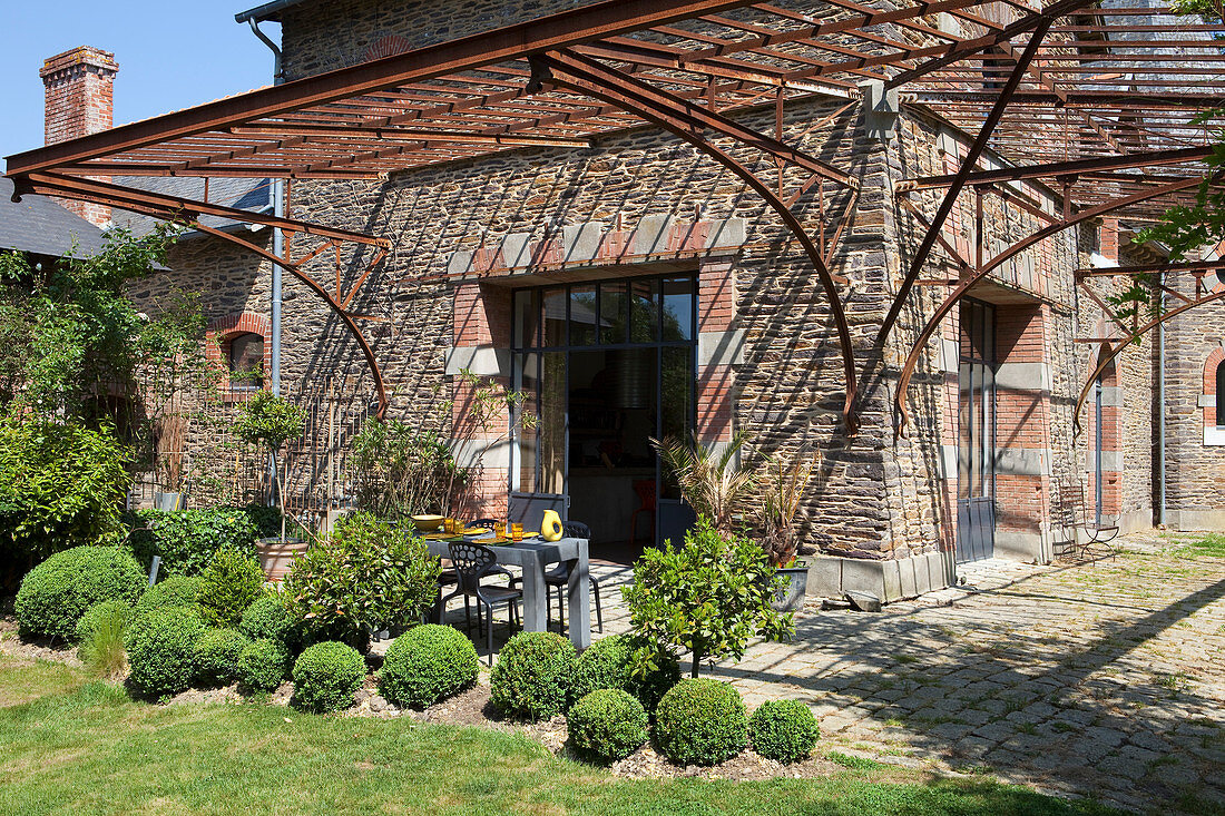 Buchsbaumkugeln vor einem Steinhaus mit Metallvordach