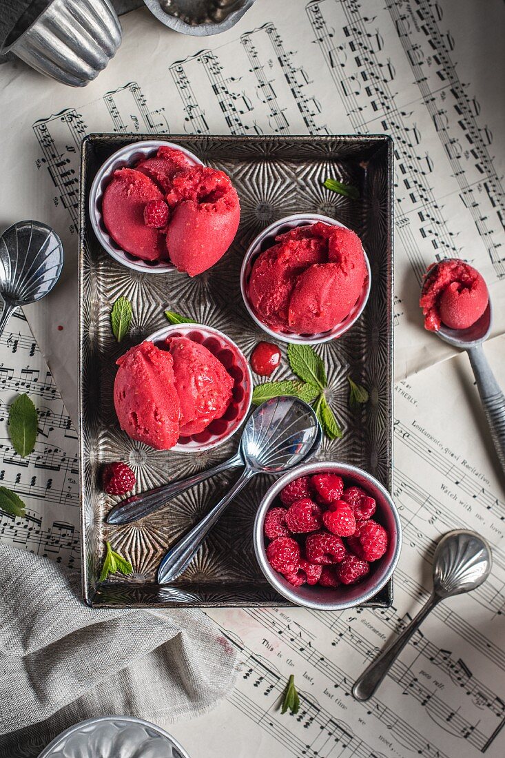 Raspberry sorbet in small bowls on a metal tray and sheet music