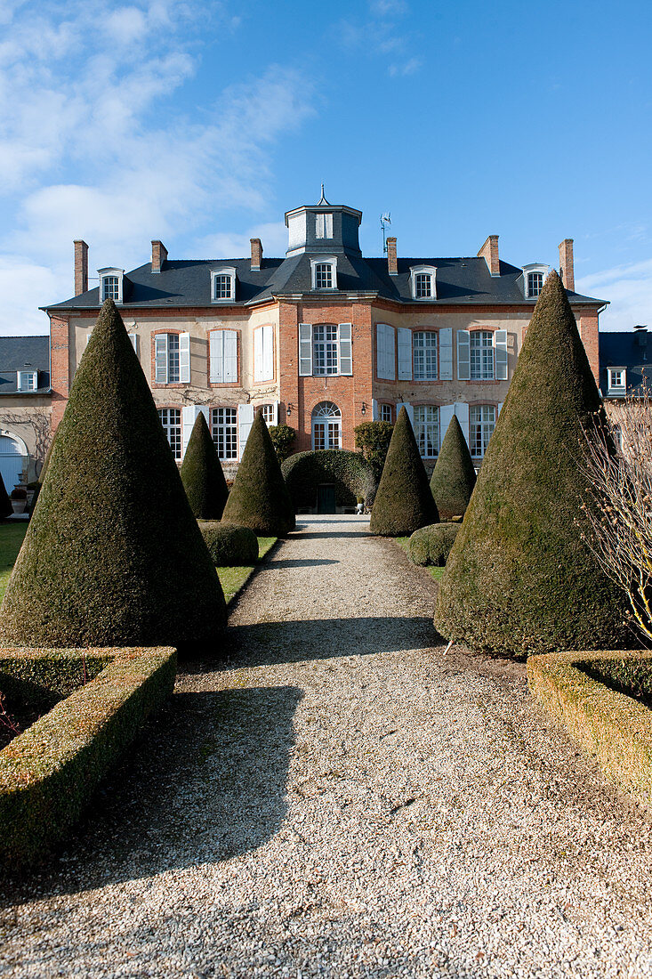 View of Château Les Aulnois between conical clipped hedges