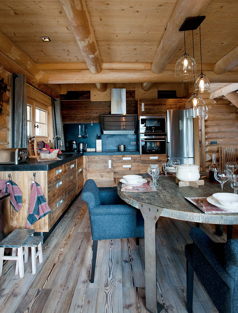 Set table in front of open-plan kitchen with wooden cupboards in log cabin