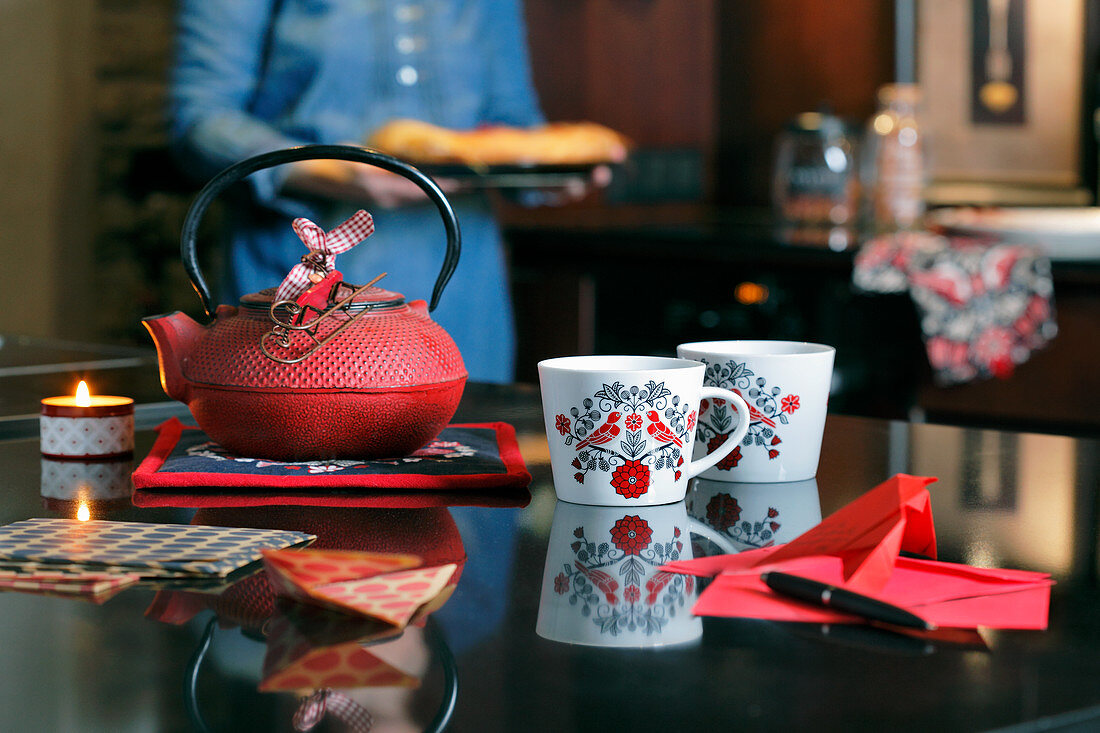 Tassen mit Vogelmotiv vor einer roten Teekanne aus Gusseisen