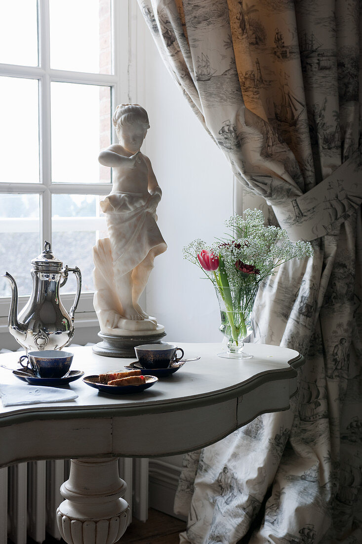 Breakfast crockery on table with baluster leg below window