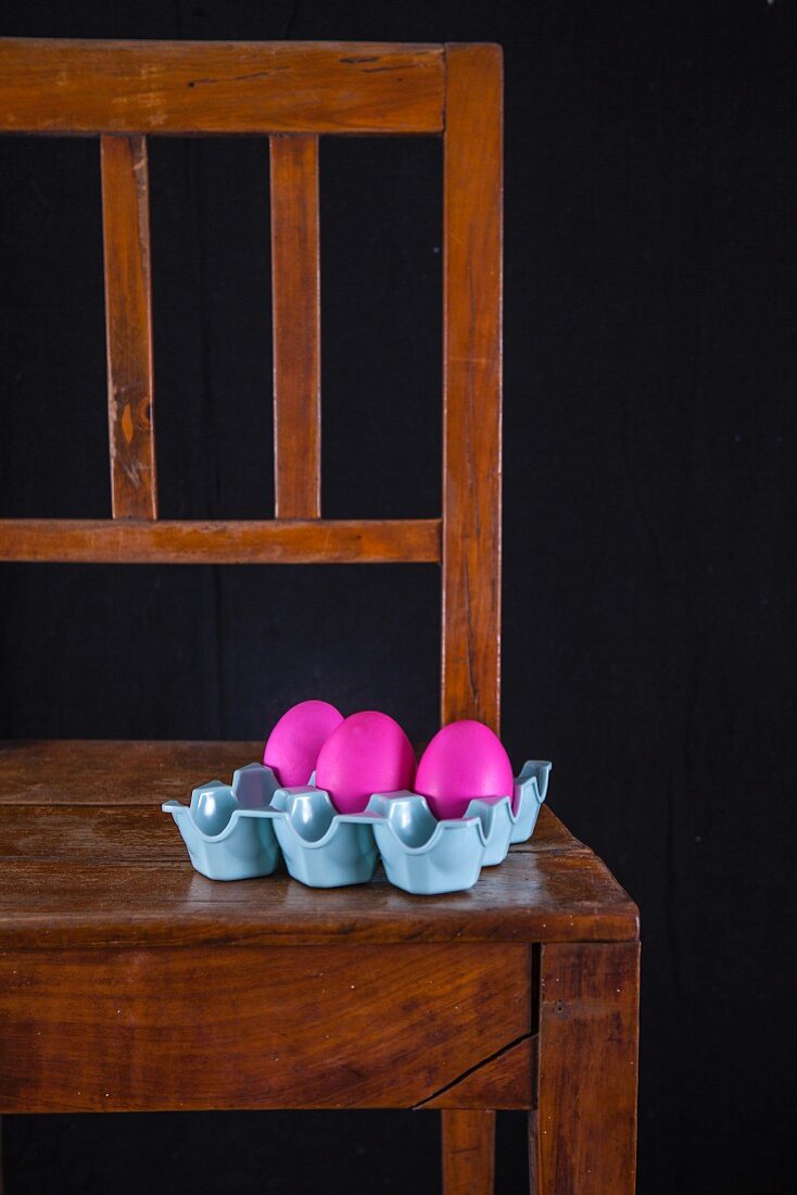 Pink Easter eggs in an egg carton on a wooden chair