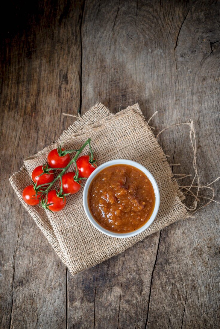 Tomatenchutney im Schälchen auf Sackleinen und Holzuntergrund