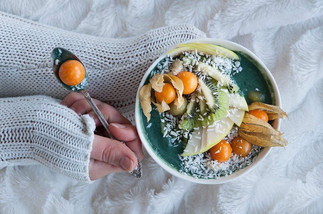 A green smoothie bowl with physalis, kiwi, apple and coconut flakes