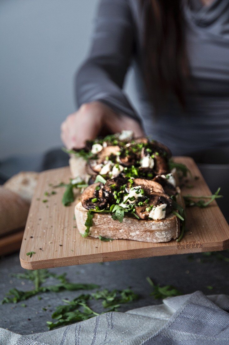 Bruschetta with mushrooms, feta and rocket on a wooden chopping board